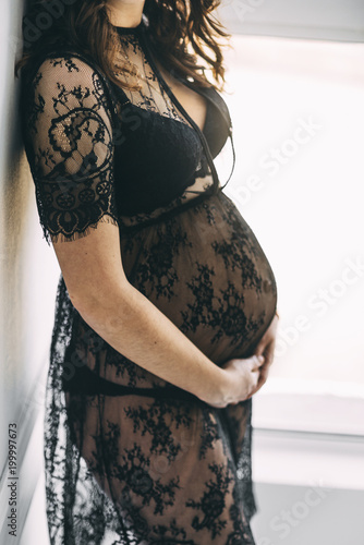 pregnant woman hugging her belly in dress sitting near the wall standing