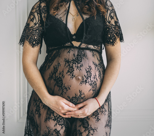 pregnant woman hugging her belly in dress sitting near the wall standing