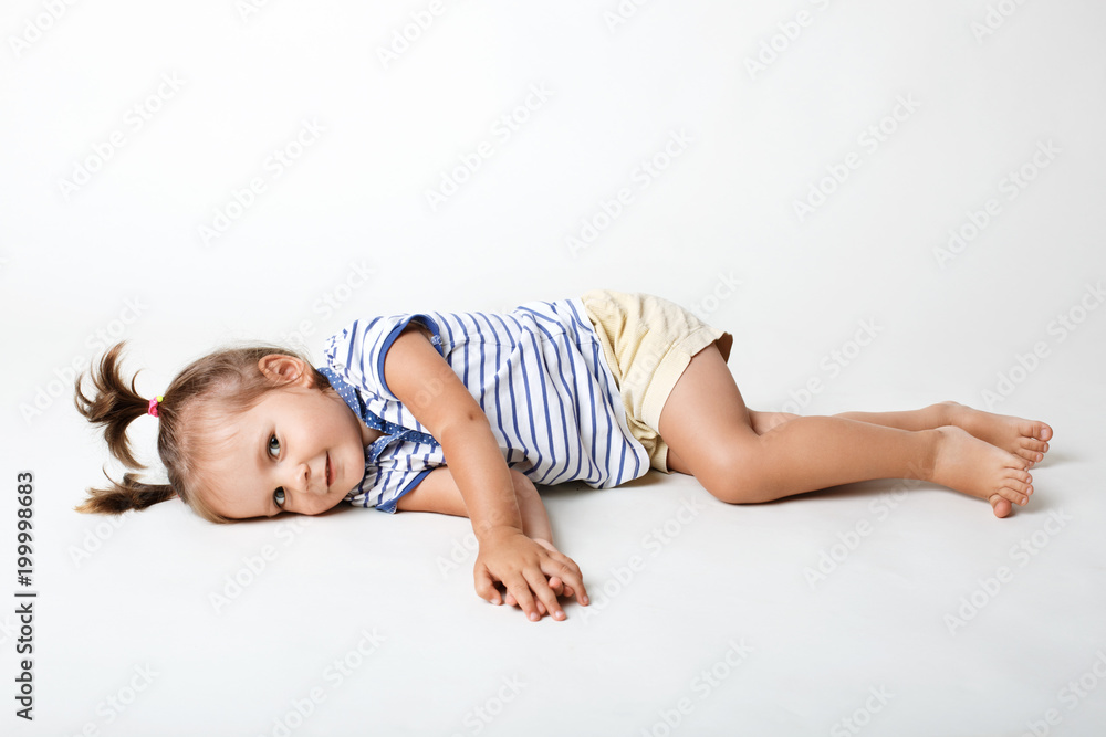 Φωτογραφία Funny small female child, wears casual t shirt and shorts, has two pony tails, looks joyfully directly into camera, isolated over white studio background