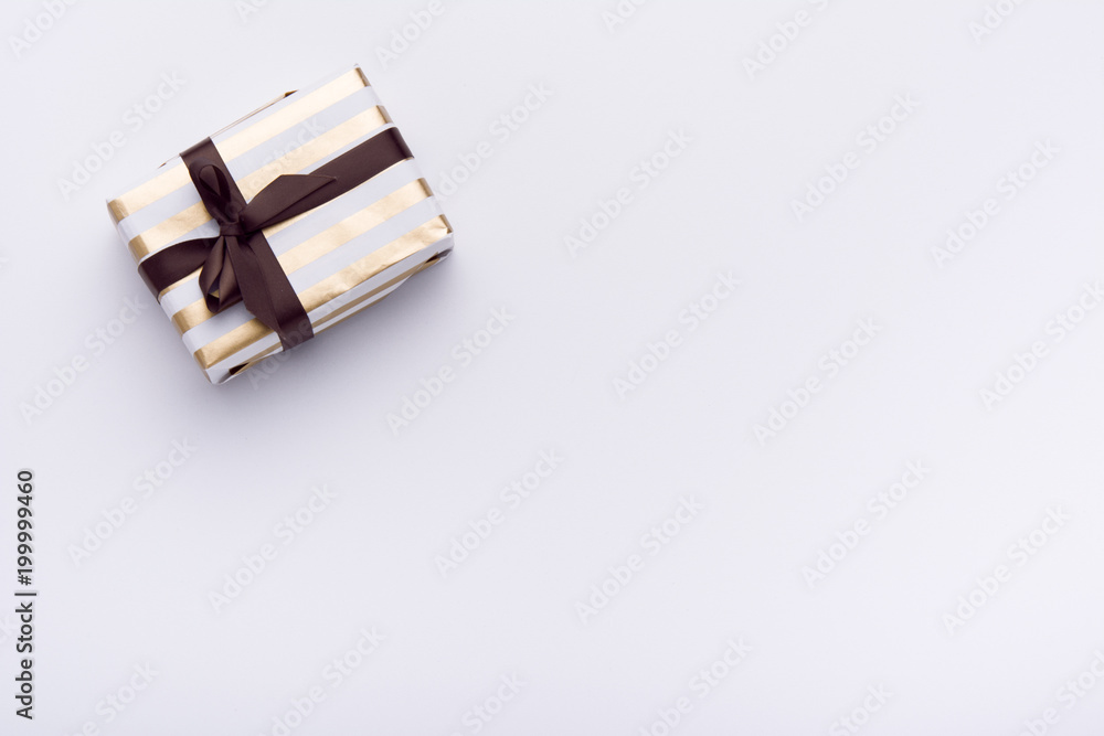 Hands holding wrapped gift box with colored ribbon as a present for Christmas, new year, mother's day, anniversary, birthday, party,  on white background, top view. Present for a colleague at work.