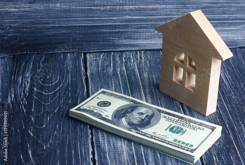 A wooden house stands next to a stack of dolor banknotes. The concept of buying and selling immovability, rent of apartments. Credit and mortgage, affordable housing. Utilities payments. photo