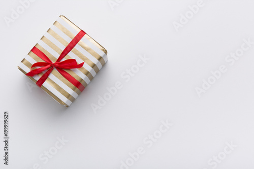 Hands holding wrapped gift box with colored ribbon as a present for Christmas, new year, mother's day, anniversary, birthday, party,  on white background, top view. Present for a colleague at work. © Krystsina