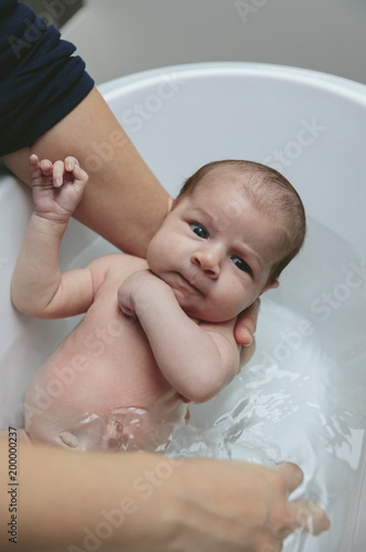 Portrait of newborn girl in the bathtub held by her mother