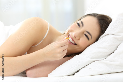 Happy girl taking pill on a bed at home
