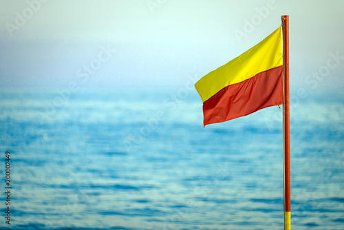Fotografie A red and yellow life saving flag against a blue sky