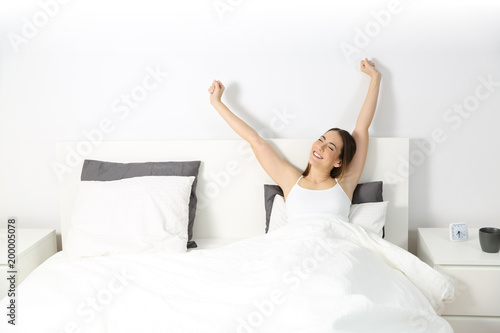 Woman waking up raising arms on the bed