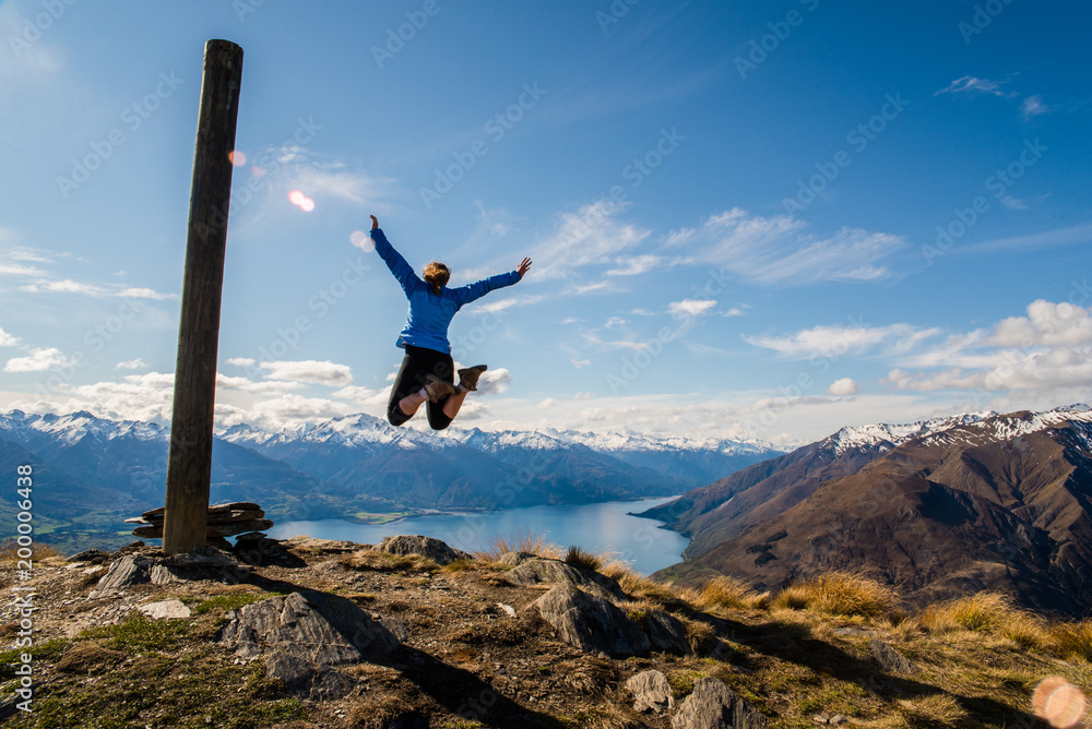 Φωτογραφία A woman jumping up in the air on the summit of a mountain with a lake in the background
