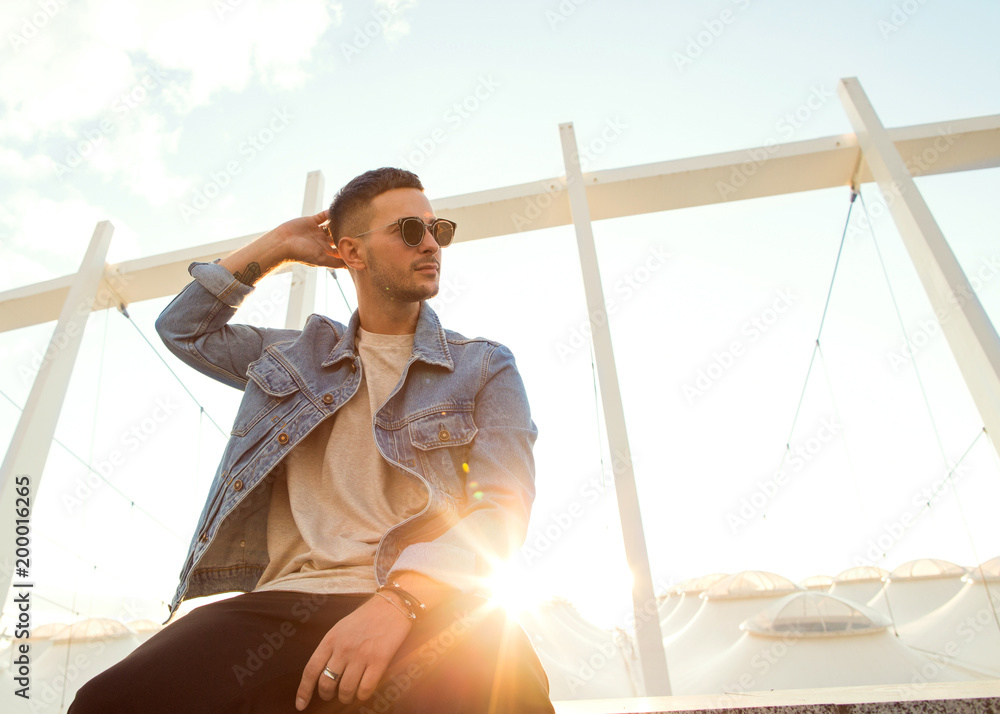 fashion guy sitting at sunset posing in sun glasses