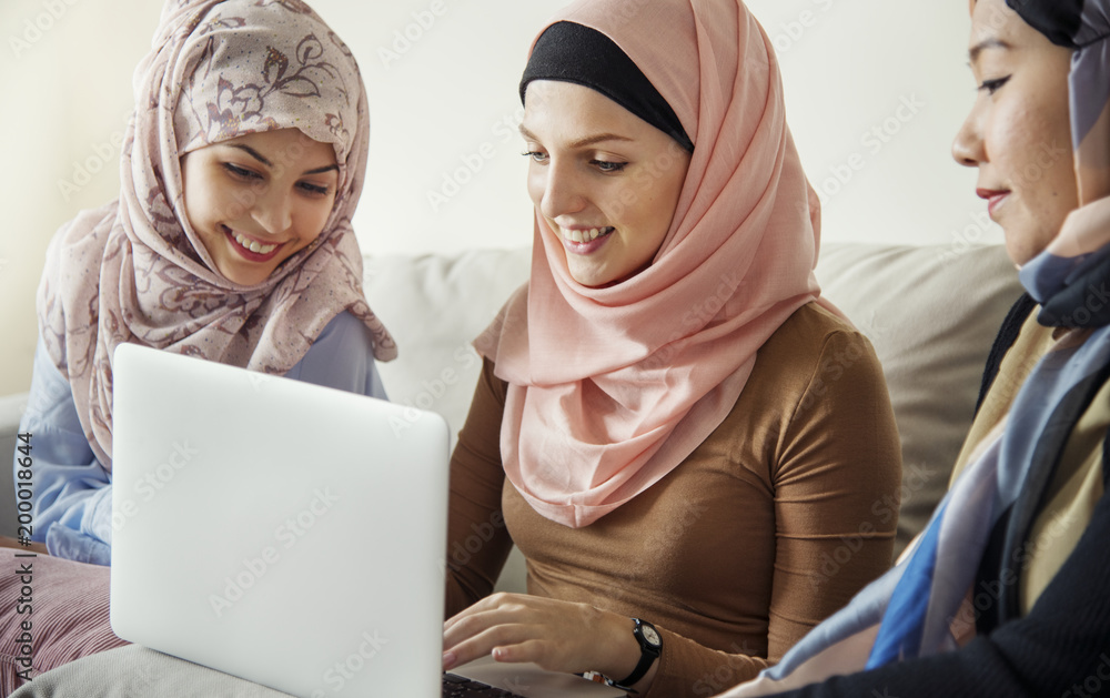 Islamic women friends sitting on the couch talking and using laptop Islamic women friends sitting on the couch talking and using laptop
