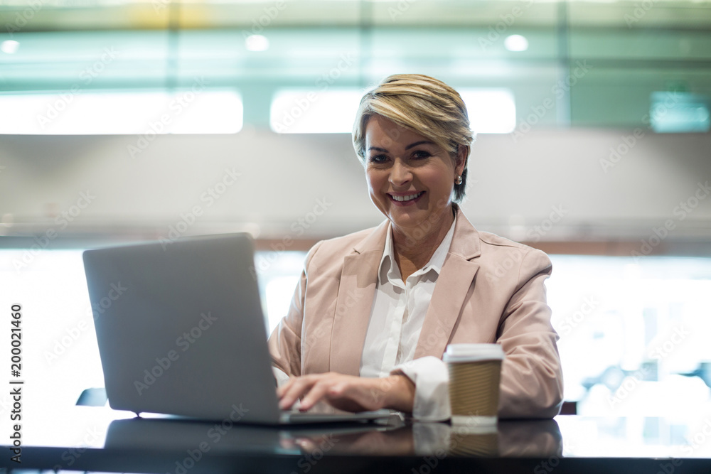 Portrait of smiling businesswoman using laptop in waiting area Portrait of smiling businesswoman using laptop in waiting area