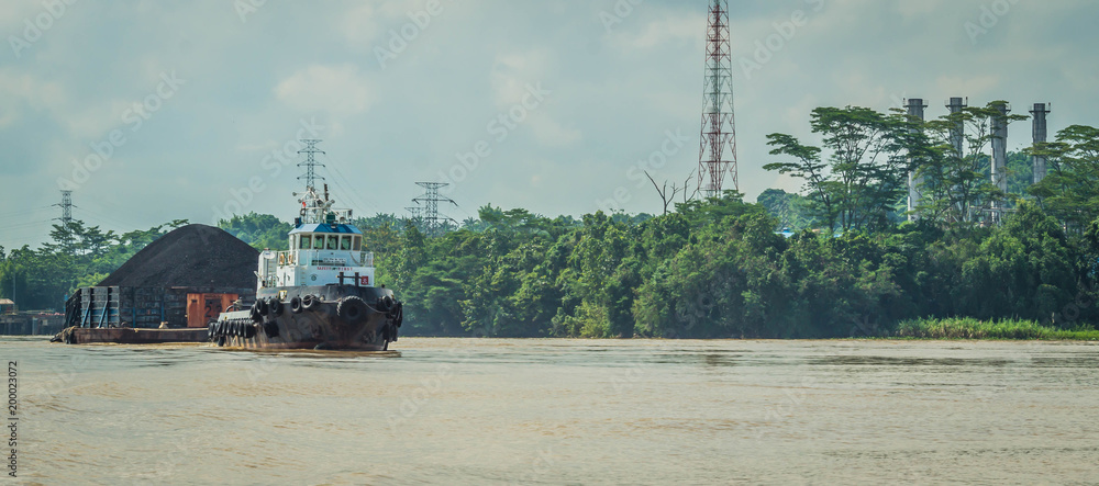 tugboat pulling heavy loaded barge of black coal in the Mahakam river ...