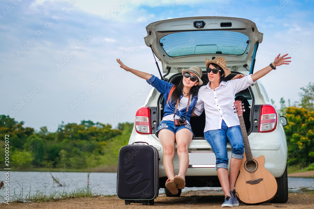 Wall Mural Couple of traveler sitting on hatchback of car and enjoy for view of nature near the lake during holiday