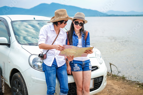 Couple of traveler standing in front of car and using a local map near the lake during holiday.Young couple tourist enjoying on vacation. 