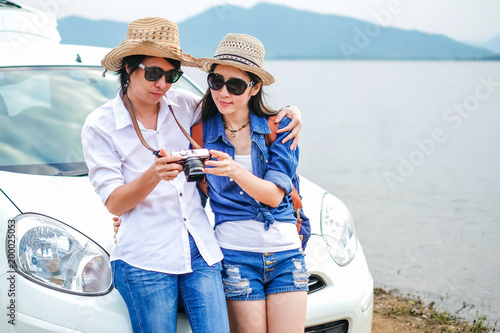 Couple of traveler standing in front of car and looking at the picture on camera near the lake during holiday.Young couple tourist enjoying on vacation. 