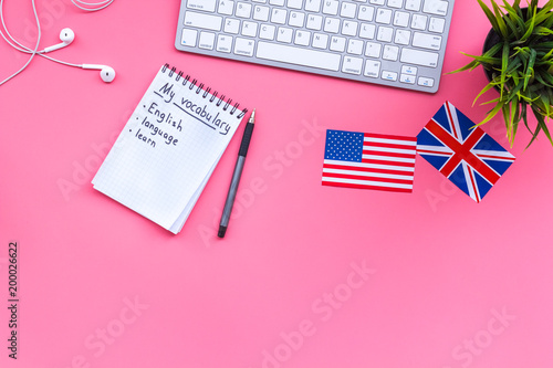 Learn new english vocabulary. Learn landuage concept. Computer keyboard  british and american flags  notebook for writing new vocabulary on pink background top view copy space