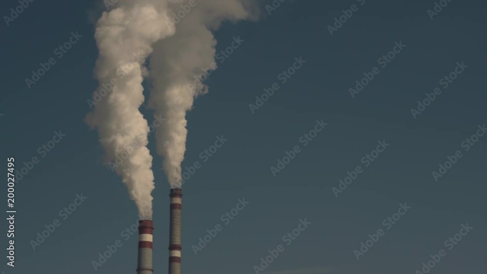Concept Of Environmental Pollution Or Industry. Slow Motion White Smoke Comes From Two Large Pipes Against A Blue Sky On A Sunny Day Concept Of Environmental Pollution Or Industry. Slow Motion White Smoke Comes From Two Large Pipes Against A Blue Sky On A Sunny Day