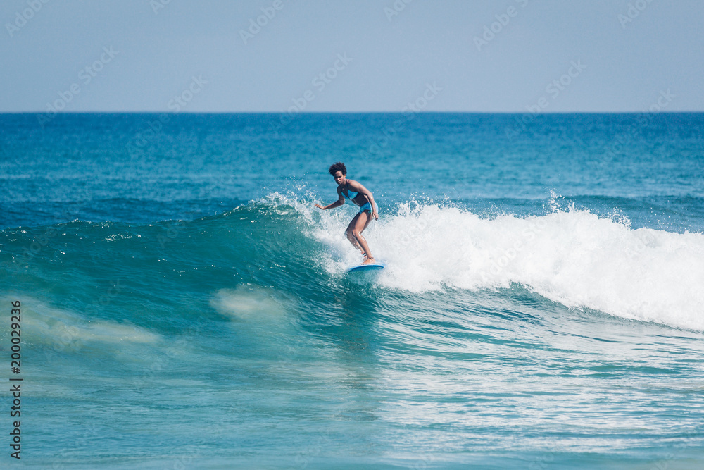 Pacific islander surfer girl with afro surfing on longboard in Padang Padang beach, Bali
