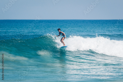 Pacific islander surfer girl with afro surfing on longboard in Padang Padang beach, Bali