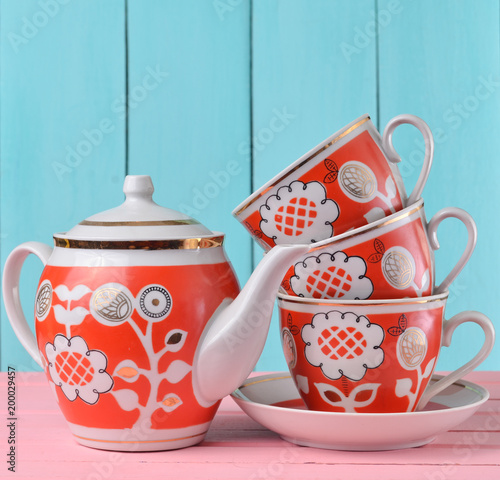 A stack of ceramic retro cups with red patternsand teapot on a pink wooden table against a blue wooden wall background, pastel color trend. photo