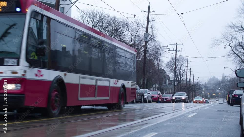 I Toronto city bus passes by on a foggy rainy day. We are on a residential street and we can see streetcar wires overhead. I Toronto city bus passes by on a foggy rainy day. We are on a residential street and we can see streetcar wires overhead.