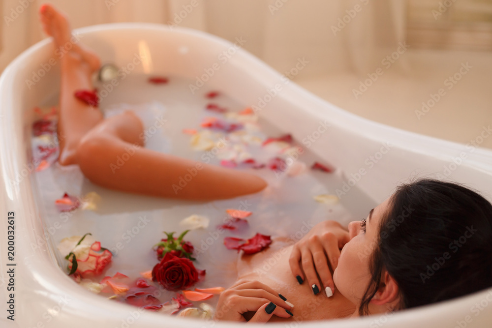 Fototapeta premium Attractive girl having a bath with milk and rose petals. Spa treatments for skin rejuvenation