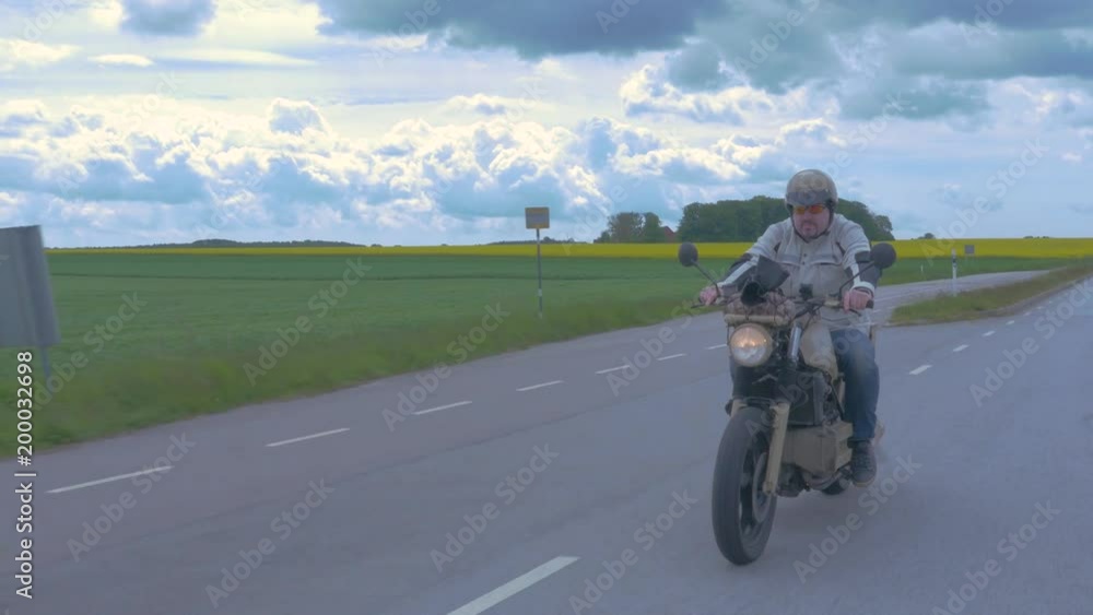 Male biker rides his motorbike down an open county road Male biker rides his motorbike down an open county road