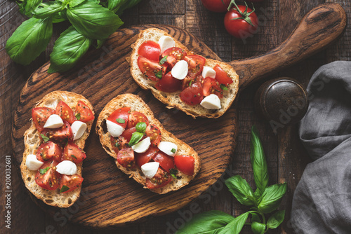 Italian bruschetta antipasti with tomatoes, mozzarella cheese and basil on wooden board. Top view, toned image