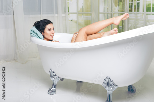 Taking care of her beautiful legs. Side view of beautiful young woman touching her leg while enjoying luxurious bath