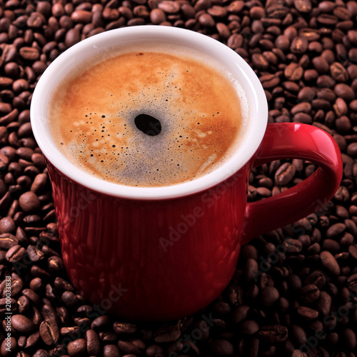 Red coffee mug filled full with espresso americano closeup against a background of scattered dark roasted beans photo