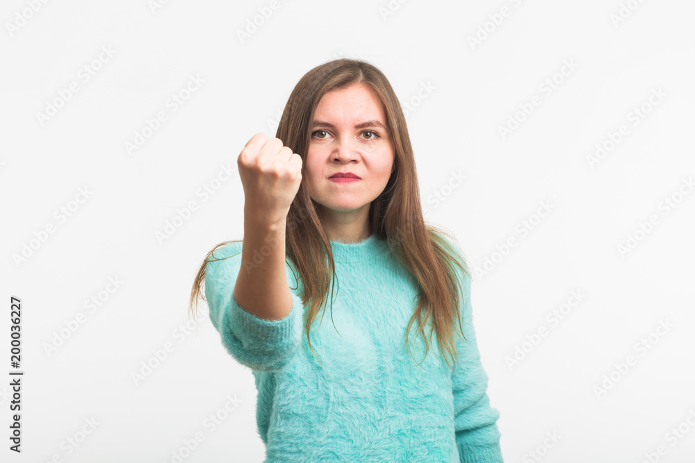 Fototapeta premium furious young brunette woman shows fist. The girl is very angry and ready to use his fists. Negative aggressive emotions on her face.
