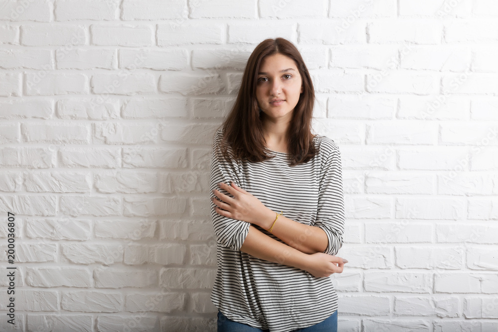 A young pretty smiling girl against a white loft-style brick wall. She looks at the viewer. Copy space. A young pretty smiling girl against a white loft-style brick wall. She looks at the viewer. Copy space.