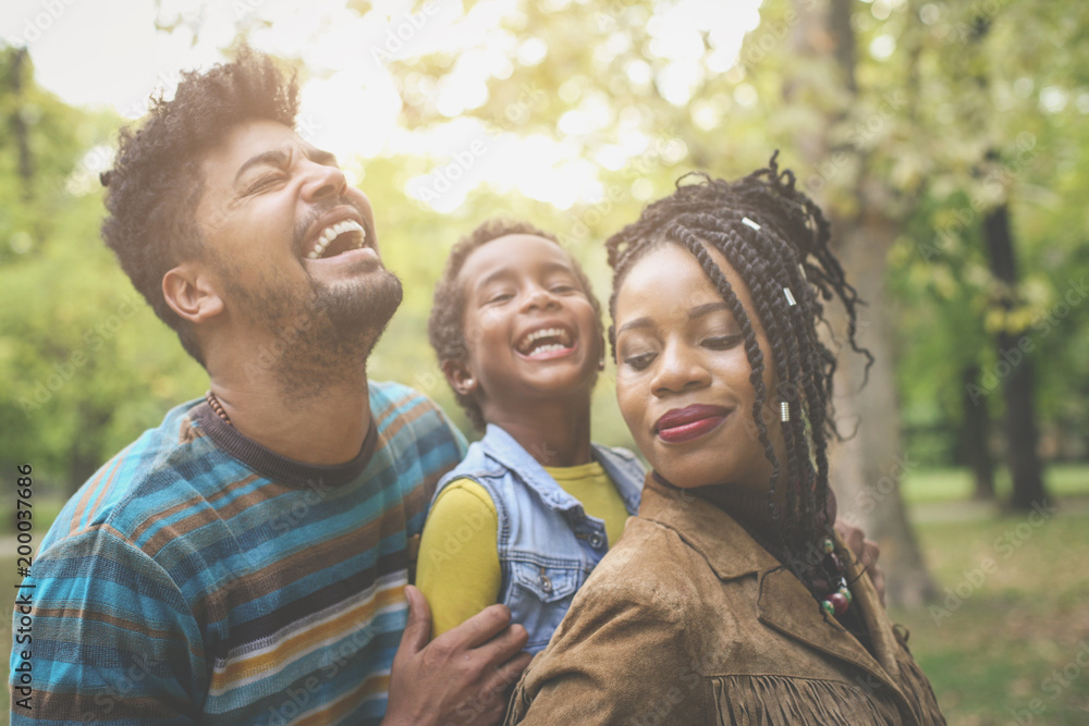 African American parents enjoying with daughter in park and laughing.