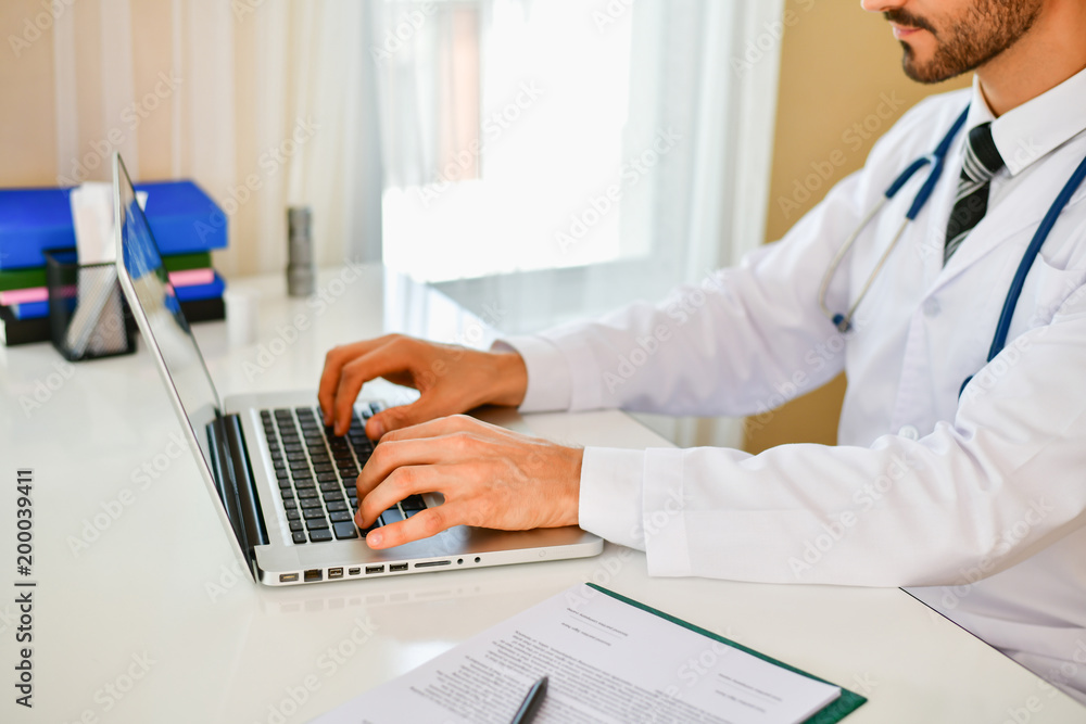 Smiling doctor posing in the office, he is wearing a stethoscope, medical staff on the hospital background Smiling doctor posing in the office, he is wearing a stethoscope, medical staff on the hospital background