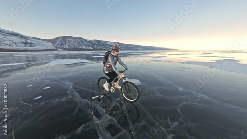 Woman is riding bicycle on the ice. The girl is dressed in a silvery down jacket, cycling backpack and helmet. Ice of the frozen Lake Baikal. The tires on the bicycle are covered with special spikes photo