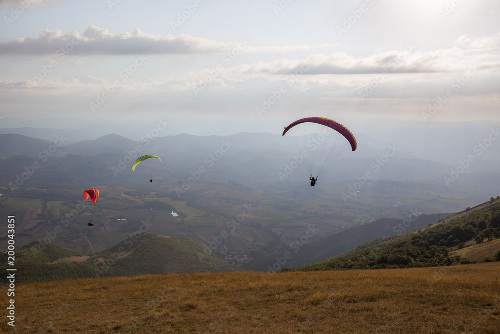 Some colorful paragliders flying over Monte Cucco (Umbria, Italy), with some faint sunrays. Some colorful paragliders flying over Monte Cucco (Umbria, Italy), with some faint sunrays.