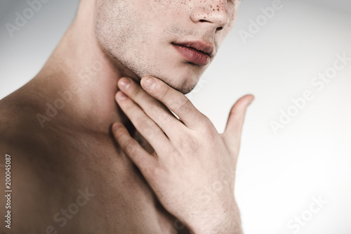 Serious undressed male holding chin by hand. He having freckles on nose. Earnest concept. Close up photo