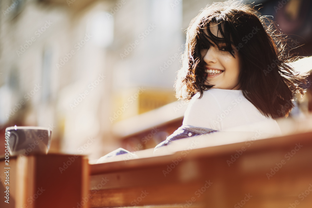 Brunette girl sitting on a bench with cup a coffee near and looking at camera. Brunette girl sitting on a bench with cup a coffee near and looking at camera.