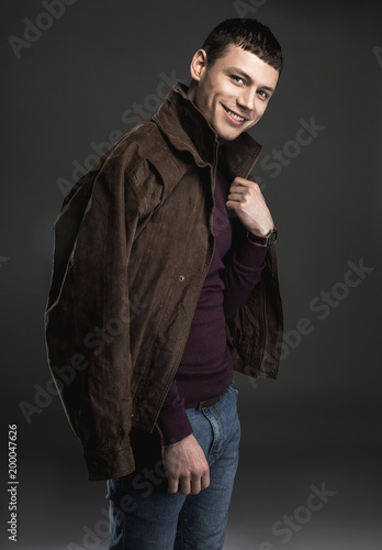 Portrait of beaming male wearing modern jacket on shoulders while looking at camera. Fashion and satisfaction concept