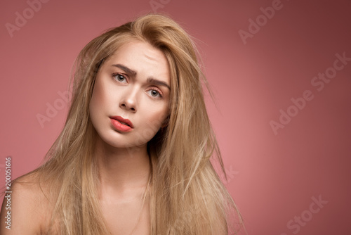 Portrait of discontent woman with untidy hair looking at camera with desperation. Copy space in right side. Isolated on rose background
