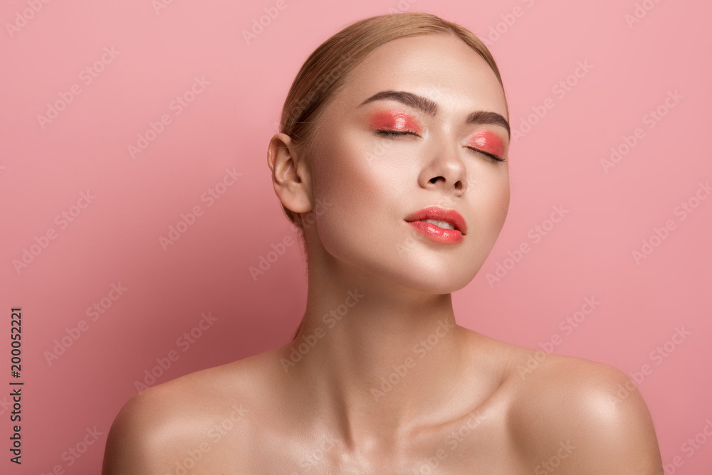 Portrait of young woman with bare shoulders and soft derma standing with eyes closed. Isolated on rose background Portrait of young woman with bare shoulders and soft derma standing with eyes closed. Isolated on rose background