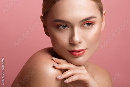 Portrait of wistful girl having cared appearance and nude cleavage. She is looking aside and touching her face with elegance. Isolated on rose background