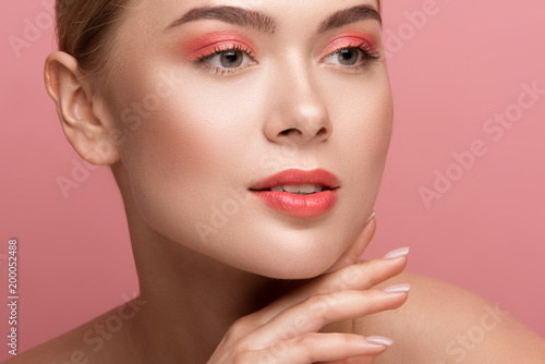Close up of peaceful female expression with light makeup looking aside. Her pelt having healthy tone. Isolated on rose background