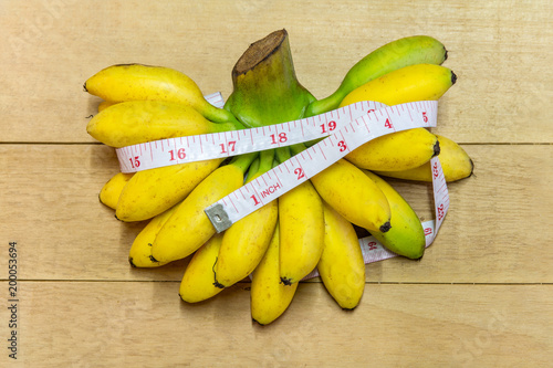 White measuring tape wrapped around banana on wooden floor, concept for eating