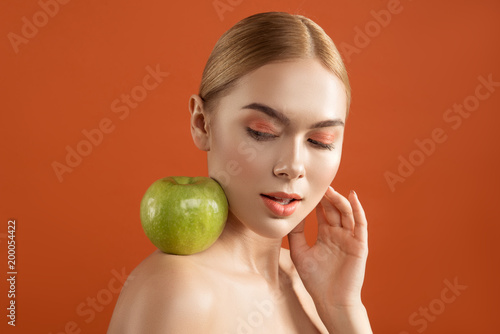 Youthfulness concept. Portrait of calm naked lady with smooth skin looking at apple on her shoulder. Isolated on background