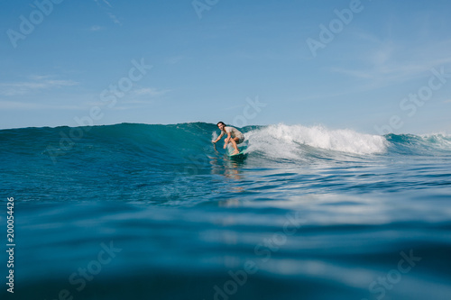 young man in wet t-shirt riding blue waves on surfboard while having vacation