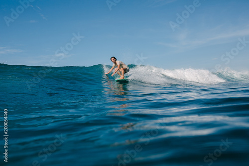 athletic man in wet t-shirt riding waves on surfboard on sunny day