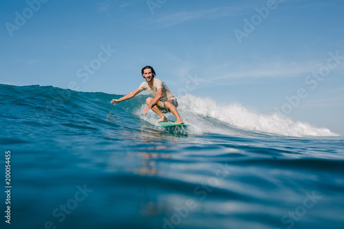 happy young man in wet t-shirt riding waves on surfboard on sunny day © LIGHTFIELD STUDIOS