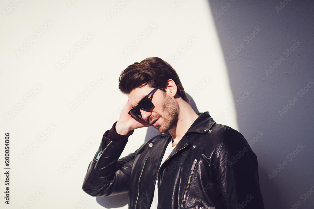 Handsome young man in leather jacket and sunglasses while standing against white background Handsome young man in leather jacket and sunglasses while standing against white background