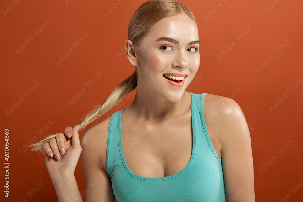 Portrait of blonde lady with neat hairdo. She is touching her ponytail and laughing. Isolated on background Portrait of blonde lady with neat hairdo. She is touching her ponytail and laughing. Isolated on background