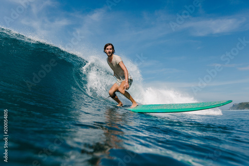 Canvas Print young man in wet t-shirt riding waves on surfboard on sunny day